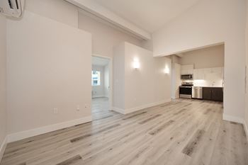 An empty living room and kitchen with white walls and wood flooring